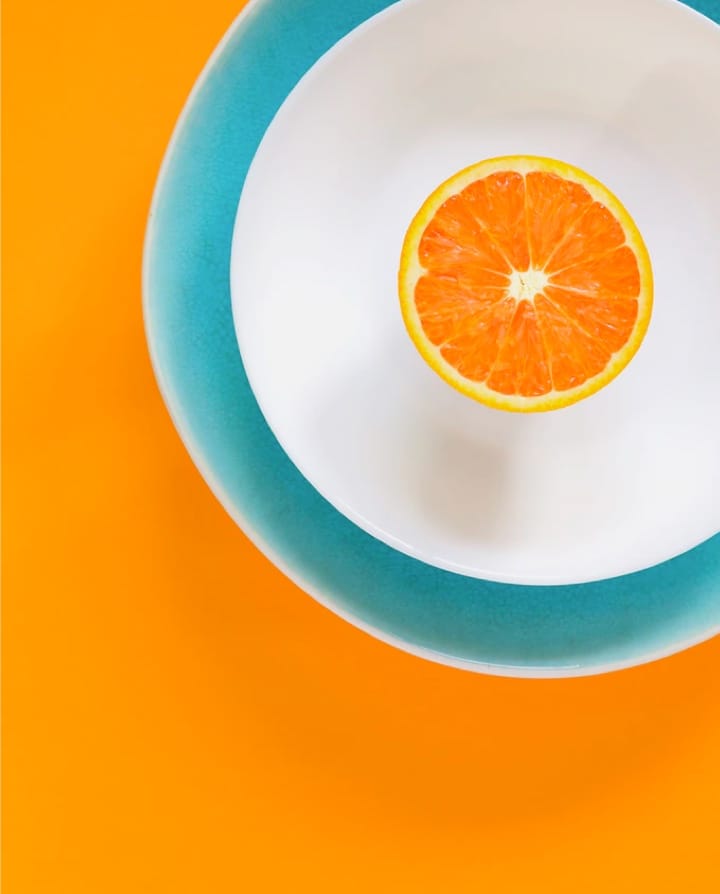 an orange in a white blue bordered plate with orange background